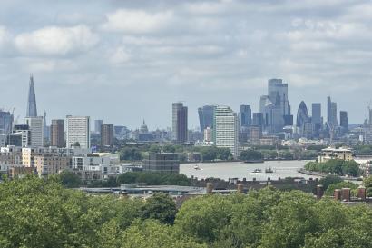 A photo of the London skyline, with green trees on the bottom and a slightly cloudy sky above.